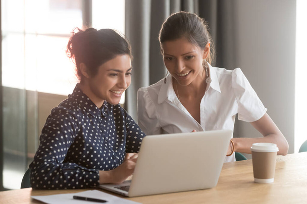 Hymyilevät monipuoliset naispuoliset työtoverit keskustelevat verkkotyöstä kannettavan tietokoneen avulla
 - Valokuva, kuva