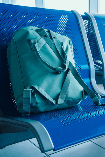 Havaalanında koltukları olan bir salon, mavi tonlu. Havaalanı terminalinde yeşil seyahat çantası. Gecikme, Tatil, Seyahat konsepti - Fotoğraf, Görsel