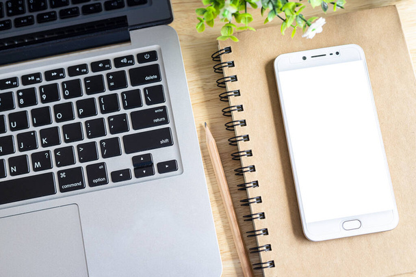laptop met smartphone op notebook, potlood en bloempot  - Foto, afbeelding