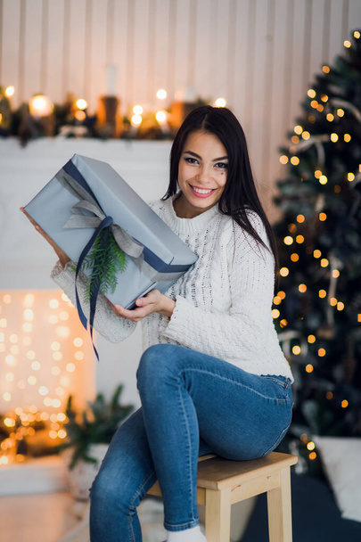 Szczęśliwa dziewczyna w podnieceniu otwiera pudełko świąteczne, próbując zgadnąć, co jest w środku. Podekscytowana kobieta. Prezent gwiazdkowy - Zdjęcie, obraz
