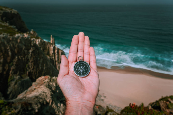 Looking at the compass in man hand palm symbolling adventure-seeking concept against sea and waves in coastline in background - Fotoğraf, Görsel