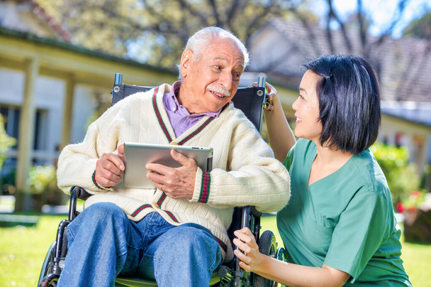 Vrouwelijke arts helpt oudere gepensioneerden met tablet in de ziekenhuistuin. - Foto, afbeelding