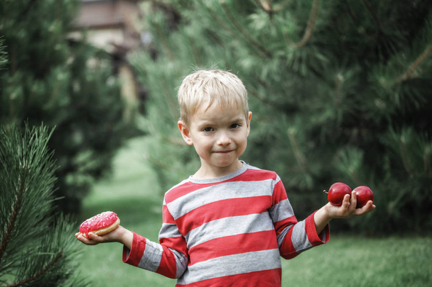 Gelukkige jongen eet een felroze donut op de weide - Foto, afbeelding