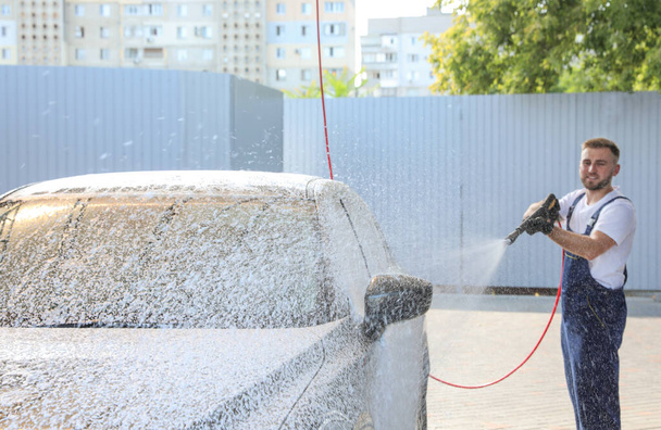 Young worker cleaning automobile with high pressure water jet at car wash - Фото, зображення