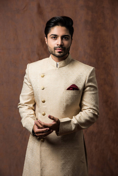 Indian man in traditional wear OR kurta / pyjama cloths.  Male fashion model in sherwani, posing / standing against brown grunge background, selective focus - Photo, Image