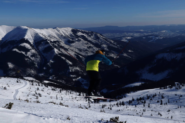 Ski rider enjoys jumping on big bump. Young teenager in colored jacket skiing on fresh powder snow with valley in background, Chopok in Slovakia Low Tatras. Acrobatic jump. Active man enjoys holiday - Photo, Image
