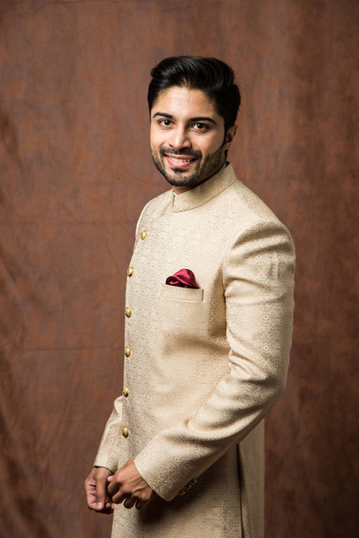Indian man in traditional wear OR kurta / pyjama cloths.  Male fashion model in sherwani, posing / standing against brown grunge background, selective focus - Фото, изображение