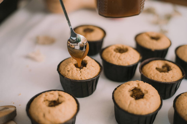 El panadero crea cupcakes en moldes. Rellenar galletas con caramelo líquido casero
 - Foto, imagen