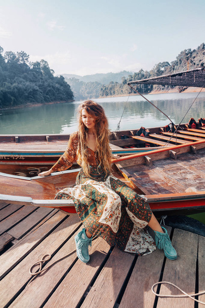 fashionable young model in boho style dress lying on boat  - Фото, изображение