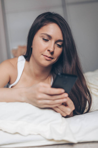 Young woman with smartphone texting message in bed at home - Foto, imagen