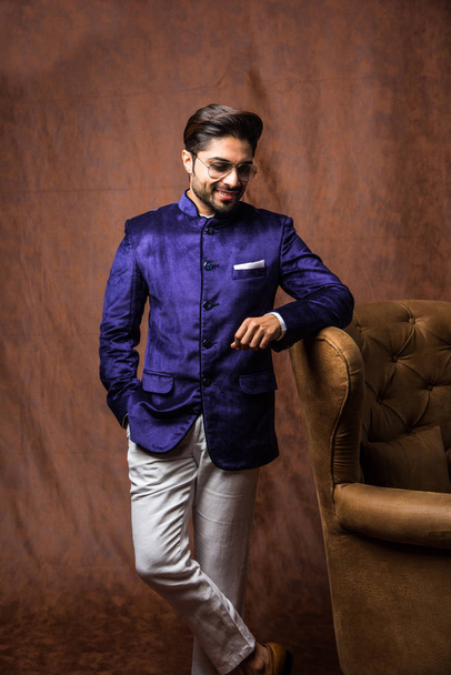 Intialainen mies käyttää etnisiä tai perinteisiä liinoja, muotimalli violetti takki ja valkoiset housut, poseeraa ruskea grunge tausta, valikoiva painopiste
 - Valokuva, kuva