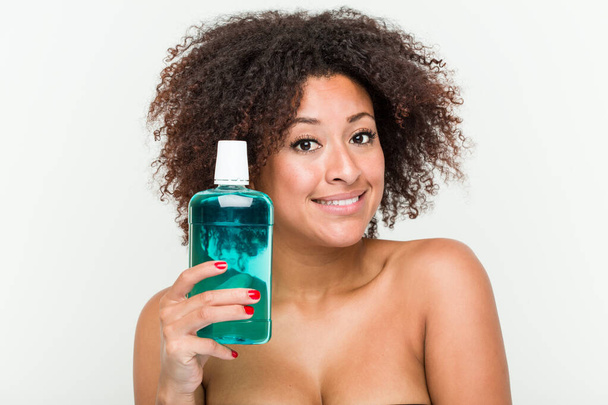 Young african american woman holding mouthwash smiling confident with crossed arms. - Foto, immagini
