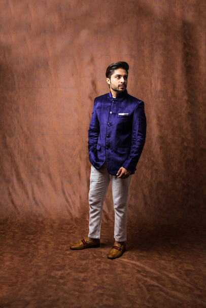 Indian Man nosí etnické nebo tradiční oblečení, módní model s fialovým kabátem a bílými kalhotami, pózuje přes hnědé grunge pozadí, selektivní zaměření - Fotografie, Obrázek