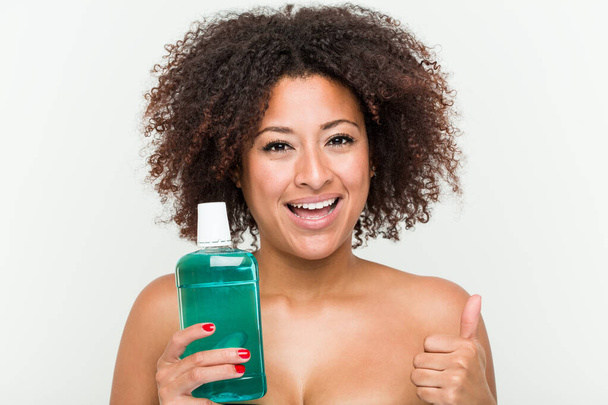 Young african american woman holding mouthwash smiling and raising thumb up - Photo, Image