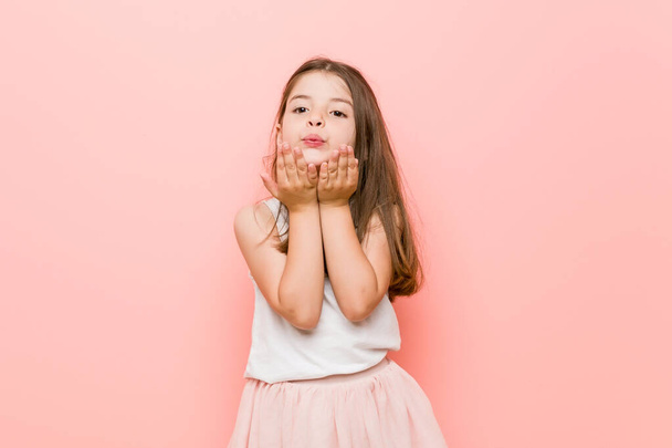 Little girl wearing a princess look folding lips and holding palms to send air kiss. - Fotó, kép