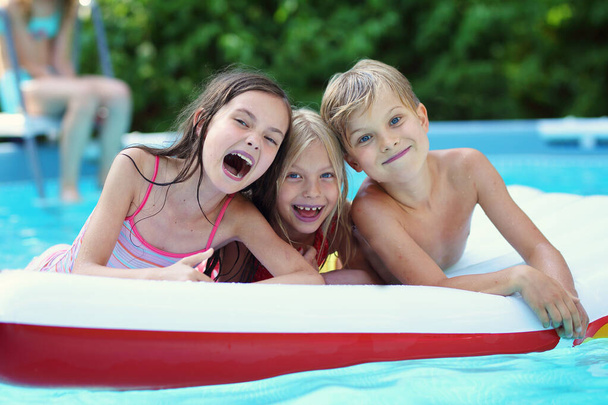 pienet lapset iloitsevat uima-altaassa kuumana kesäpäivänä
 - Valokuva, kuva