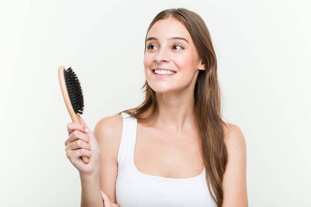Young caucasian woman holding a hair brush smiling confident with crossed arms. - Photo, Image