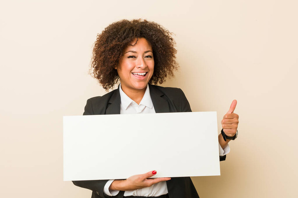 Молодая африканская американка с плакатом, улыбающаяся и поднимающая большой палец
 - Фото, изображение