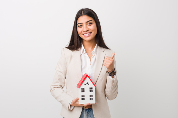 Young arab woman holding a house icon smiling and raising thumb up - Photo, Image