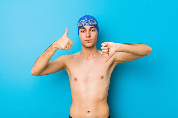 Νεαρός κολυμβητής δείχνει τους αντίχειρες και τους αντίχειρες κάτω, δύσκολη επιλογή έννοιας - Φωτογραφία, εικόνα