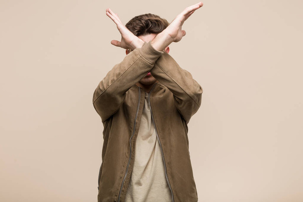 Young caucasian man wearing a brown jacket keeping two arms crossed, denial concept. - Foto, Imagem