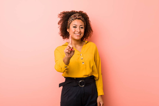 Young african american woman against a pink background showing number one with finger. - Foto, Bild