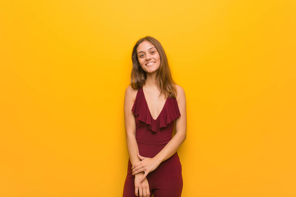 Young natural woman wearing a red dress against an orange wall - Фото, изображение