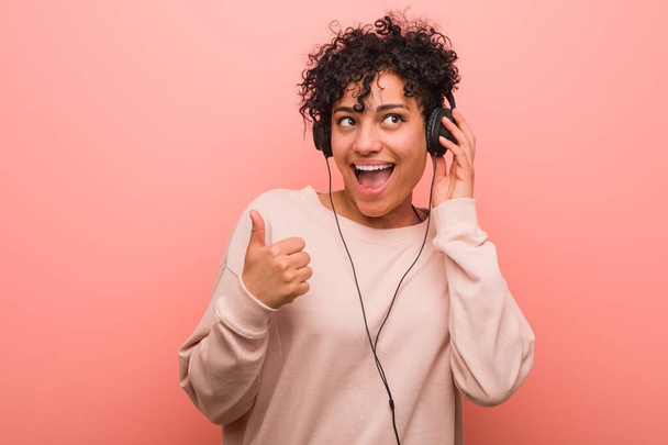 Mujer afroamericana joven escuchando música sonriendo y levantando el pulgar hacia arriba
 - Foto, imagen