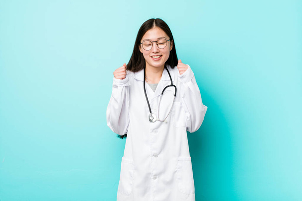 Joven doctora china levantando puño, sintiéndose feliz y exitosa. Concepto de victoria
. - Foto, Imagen