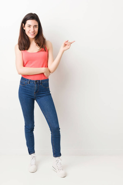 Full body young woman on white background smiling cheerfully pointing with forefinger away. - Fotoğraf, Görsel