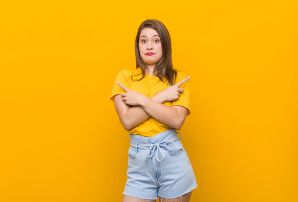 Молодая женщина подросток в желтой рубашке указывает в сторону, пытается выбрать между двумя вариантами
. - Фото, изображение