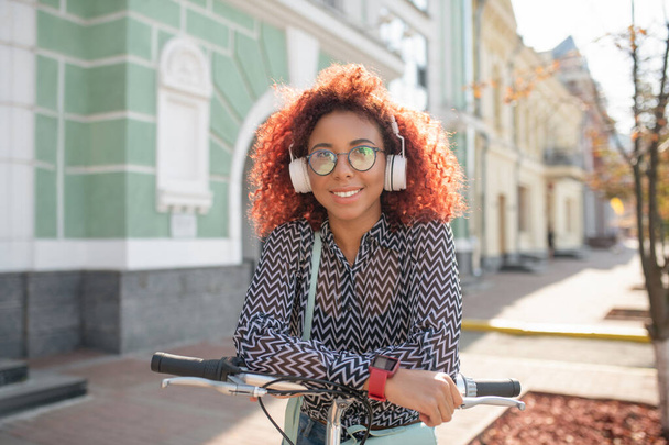 Girl wearing earphones. Young girl wearing earphones standing near her bike outside while waiting for friend - Foto, Bild