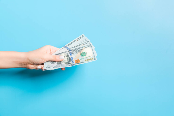 Imagen de la mano femenina sosteniendo un paquete de dólares sobre fondo azul. Concepto de pago
 - Foto, Imagen