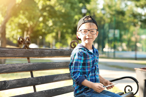Симпатичный маленький мальчик с планшетным компьютером сидит на скамейке в парке
 - Фото, изображение