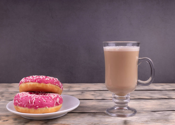 Une tasse de café en verre et deux beignets glacés roses sur fond sombre
 - Photo, image