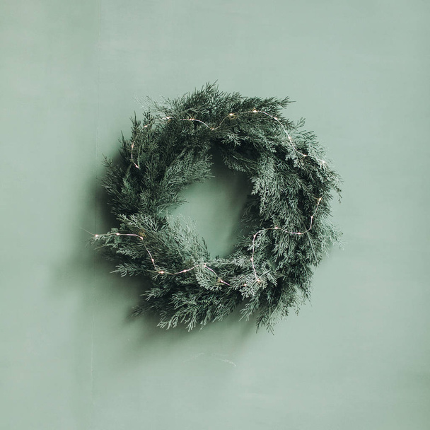 クリスマス/新年の作曲。クリスマスツリー、淡い緑の壁に対するモミの枝で作られたお祭りの花輪。最低冬休みのコンセプト. - 写真・画像