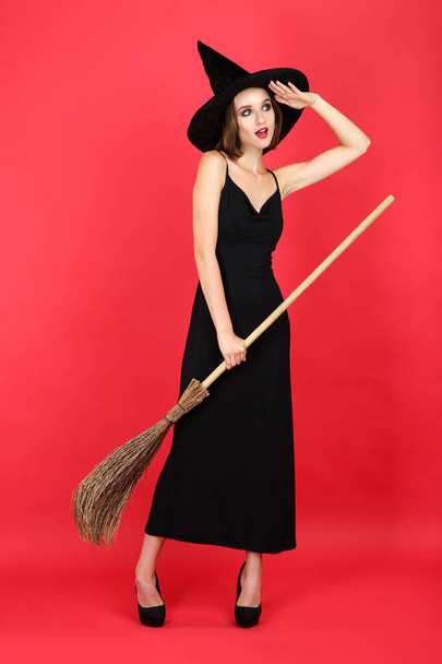 Happy young woman in black halloween costume with broom on red b - Valokuva, kuva