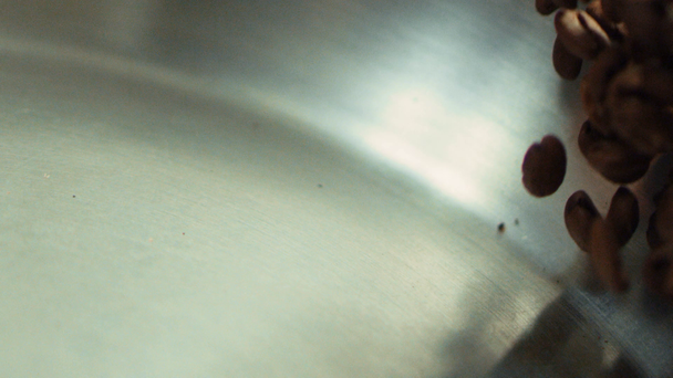 Macro of coffee beans tossing on metal pan in slow motion. Roasted coffee seeds - Кадры, видео
