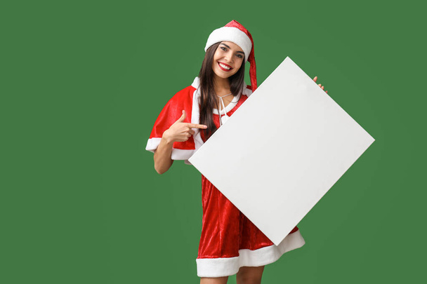 Чудова молода жінка в костюмі Санта Клауса і з чистим плакатом на кольоровому фоні. - Фото, зображення