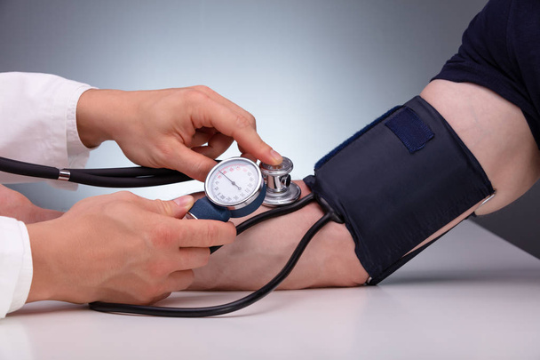 Close-up Of Doctor Checking Blood Pressure Of The Male Patient On Table Against Gray Background - Фото, изображение