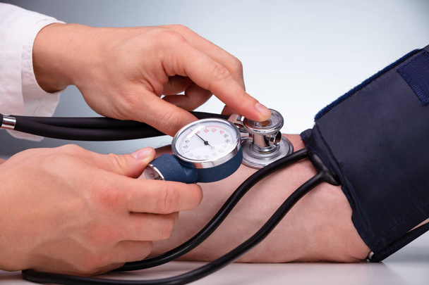 Close-up Of Doctor Checking Blood Pressure Of The Male Patient On Table Against Gray Background - Foto, immagini