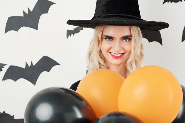 Cadı şapkası süsleme odasında kırmızı ve turuncu balonlar ve yarasa çıkartmalarıyla güzel genç bir kadın. - Fotoğraf, Görsel