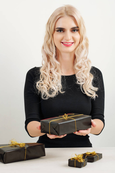 Portrait of young positive woman showing gifts she wrapped in black paper with golden ribbon - Foto, afbeelding