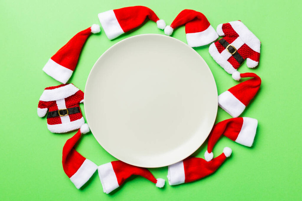Conjunto festivo de placa decorada com chapéu de Papai Noel sobre fundo colorido. Top vista conceito de jantar de Natal - Foto, Imagem