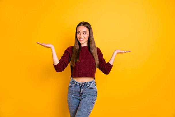 Portrait of lovely girl looking at her palms smiling wearing maroon pullover isolated over yellow background - Foto, afbeelding