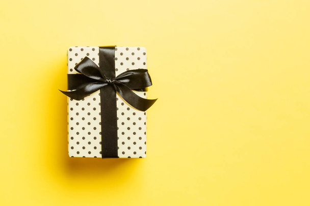 verpakt Kerstmis of andere met de hand gemaakte vakantie cadeau in papier met zwart lint op gele achtergrond. Aanwezig doos, decoratie van geschenk op gekleurde tafel, bovenaanzicht met kopieerruimte - Foto, afbeelding
