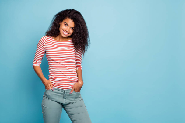 Photo of amazing pretty dark skin lady with adorable smile holding hands in pockets wear casual street clothes isolated pastel blue color background - 写真・画像