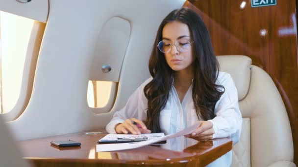 Business lady working with paper documents while aircraft flying. Businesswoman traveling in private jet plane. Rich girl flying on airplane in business class. - Video