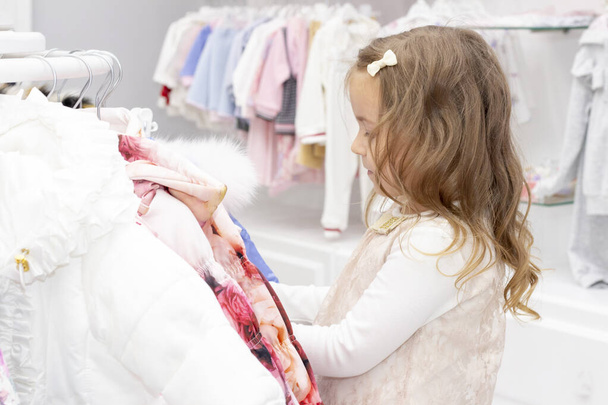 shopping. discounts. little girl shopaholic. girl delighted with beautiful jackets, chooses warm clothes. shopping center, shopping. emotions - Zdjęcie, obraz
