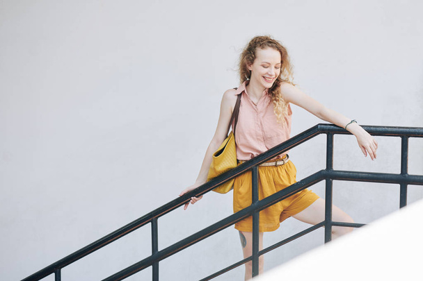 Szczęśliwy śmiech ładna dziewczyna opierając się na balustradzie i patrząc w dół ze schodów - Zdjęcie, obraz